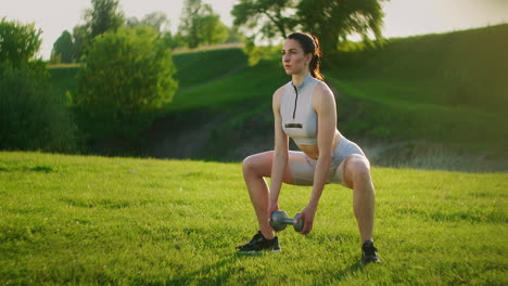 The-view-from-the-side-of-the-women's-squats-with-weight.-One-woman-trains-in-the-park-in-the-morning